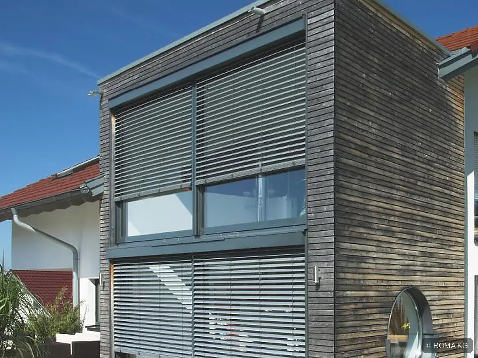 ROMA Raffstores mit gekippten Lamellen an einem Haus mit dunkler Holzfassade