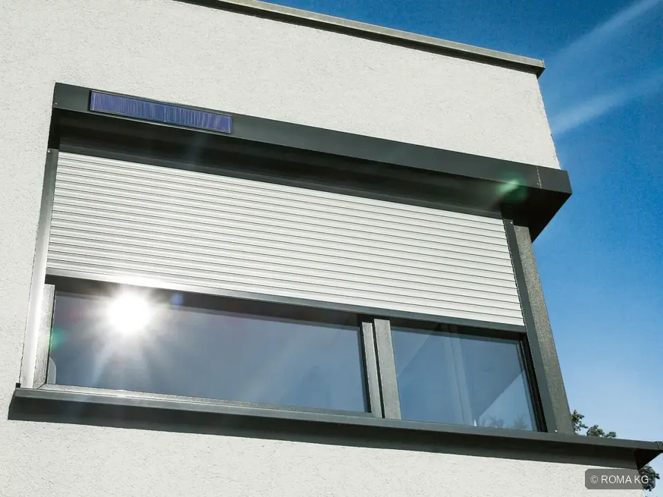 ROMA Vorbaurollladen mit Solarmodul an einer hellen Putzfassade, halb heruntergelassen